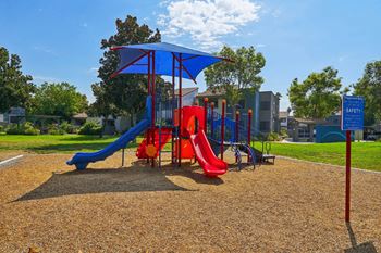 A playground with a blue umbrella and a red slide.